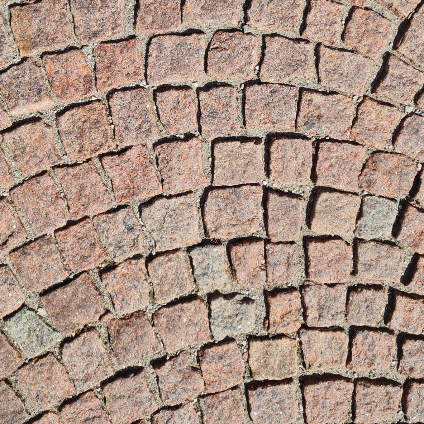 Natursteinboden aus unregelmäßig geformten Steinen in verschiedenen warmen Beige- und Brauntönen. Die Oberfläche der Steine ist leicht rau und strukturiert, was ihnen ein natürliches und rustikales Aussehen verleiht. Die Fugen sind gut sichtbar und verstärken das organische, handwerkliche Design. Dieser Bodenbelag eignet sich ideal für Außenbereiche wie Gehwege, Einfahrten oder Terrassen.